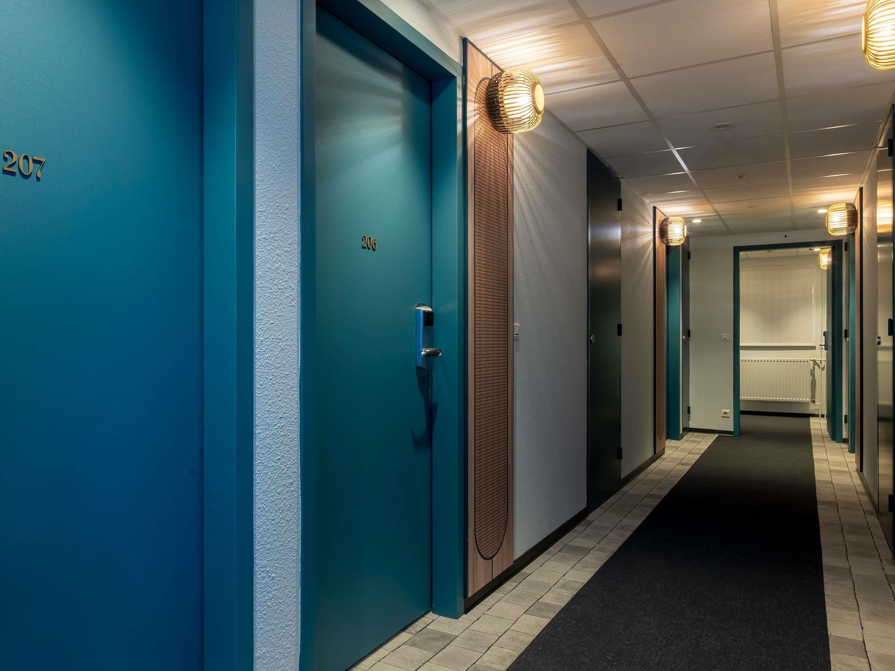 A hallway with teal-colored doors numbered 206 and 207, a textured wall, and a carpeted floor.