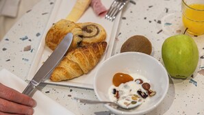 A breakfast setting with a croissant, a kiwi, an apple, and a bowl of yogurt with nuts on a speckled table. - ibis Styles Pontivy Centre Bretagne (Pontivy)
