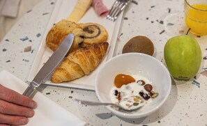 Une table de petit-déjeuner avec un croissant, un kiwi, une pomme et un bol de yaourt aux noix, le tout posé sur une table à motifs.