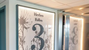 A hallway with a wall-mounted sign reading "Herbes Folles 3" and an elevator in the background. - ibis Styles Pontivy Centre Bretagne (Pontivy)