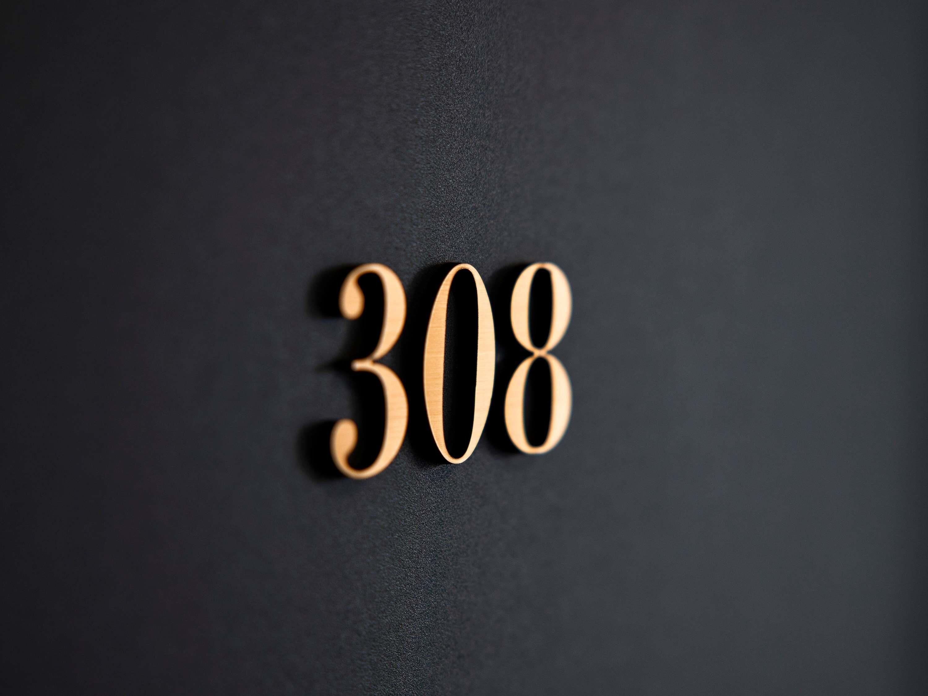 A close-up of wooden numbers '308' on a dark background.