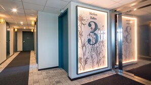 A hallway with a wall-mounted sign indicating 'Herbes Folles 3' and an elevator with a floral design. - ibis Styles Pontivy Centre Bretagne (Pontivy)