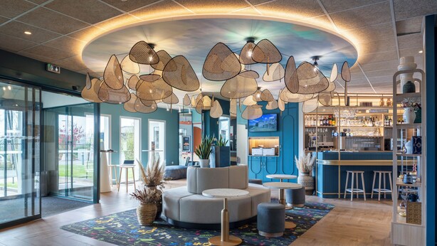 A modern lobby with a round seating area, a bar with stools, and a ceiling with unique lighting fixtures. - ibis Styles Pontivy Centre Bretagne (Pontivy)