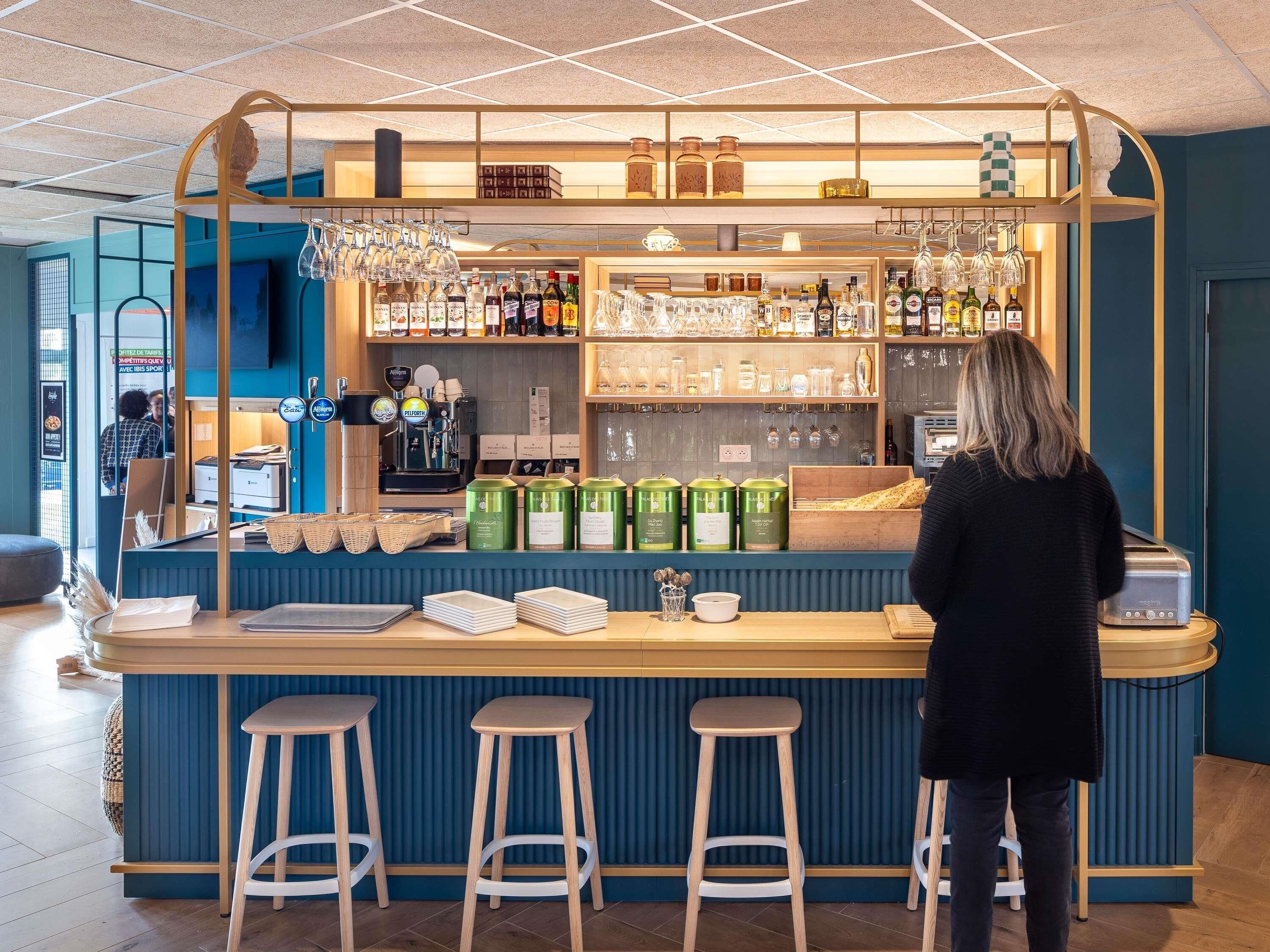 A bar area with stools, a coffee machine, and shelves stocked with bottles and glasses.
