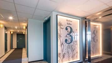 A hallway with a wall-mounted sign indicating 'Herbes Folles 3' and an elevator with a floral design.