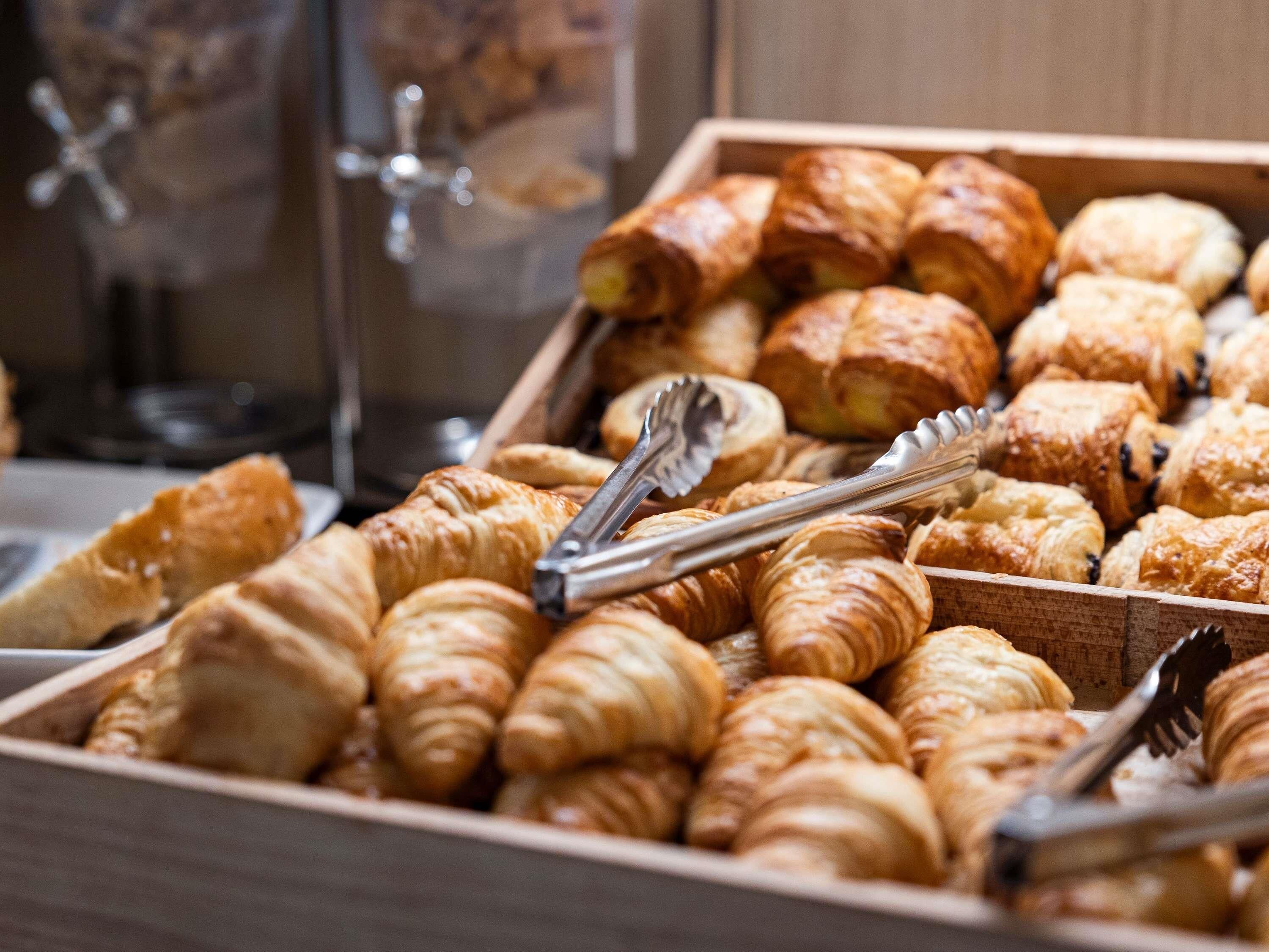 Variedad de pasteles en una caja de madera, incluyendo croissants y otras delicias horneadas.