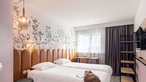 A hotel room with a bed, bedside table, lamp, and a wall with floral wallpaper. - ibis Styles Pontivy Centre Bretagne (Pontivy)