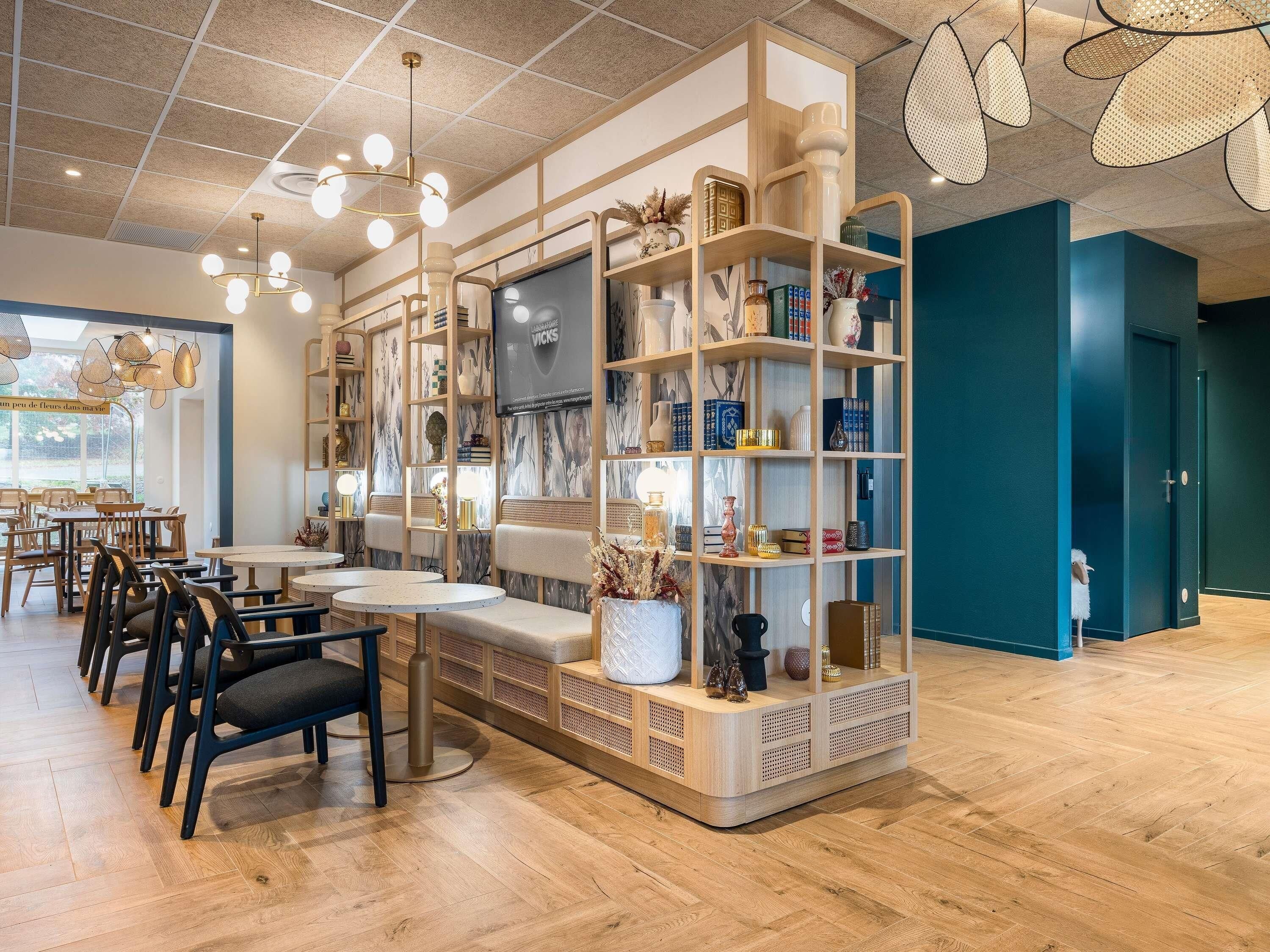 Un interior moderno con suelo de madera, mesas y sillas redondas, y una estantería central con varios objetos decorativos.