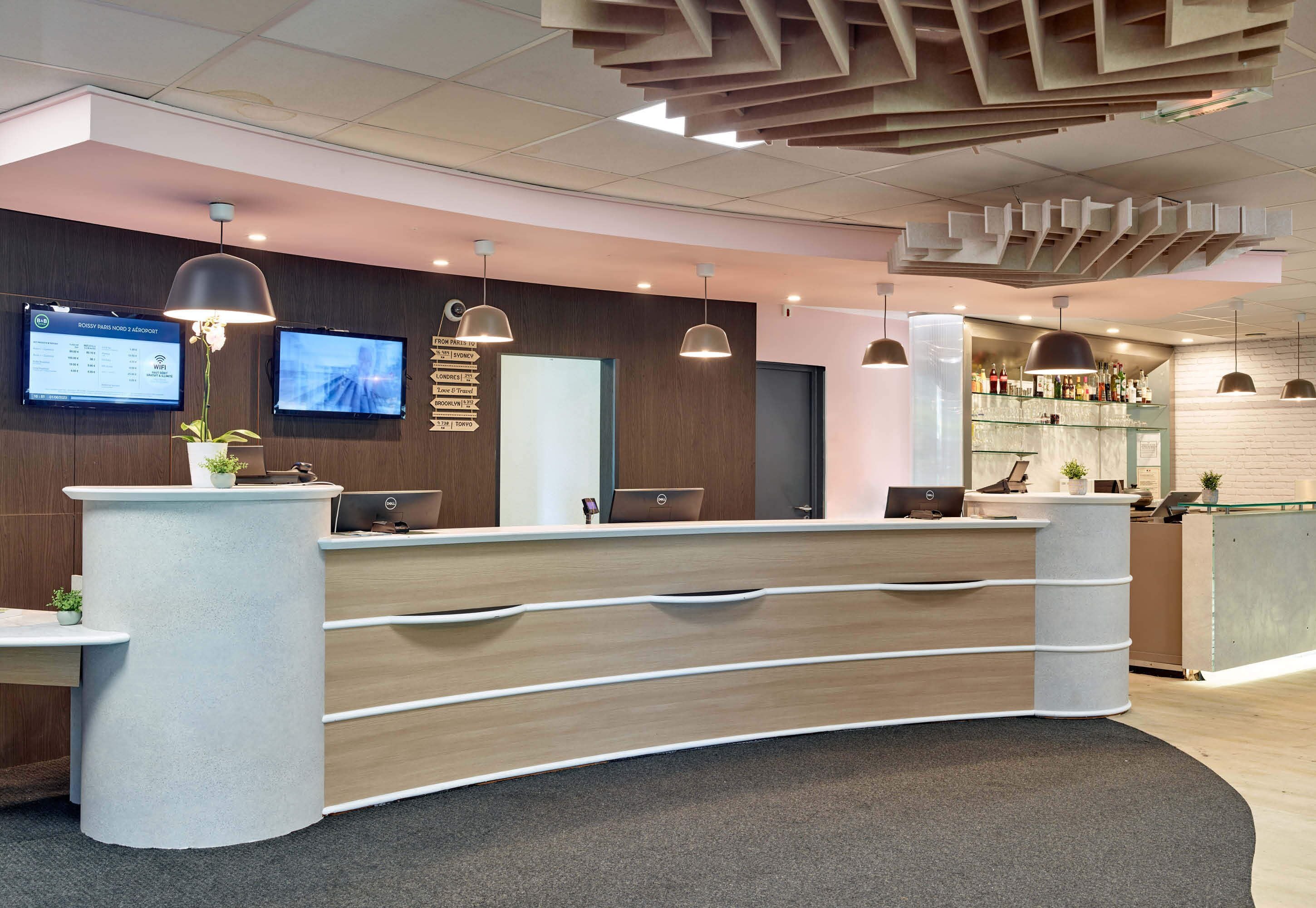 A modern reception desk with a curved design, multiple monitors, and pendant lighting.