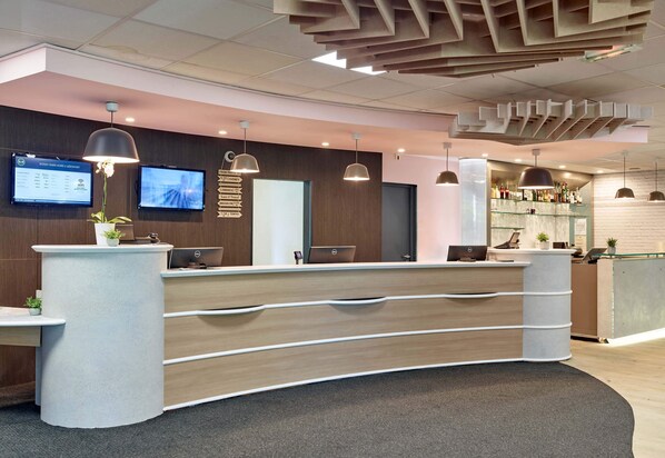 Un comptoir d’accueil moderne au design incurvé, doté de plusieurs écrans et d’un éclairage suspendu.