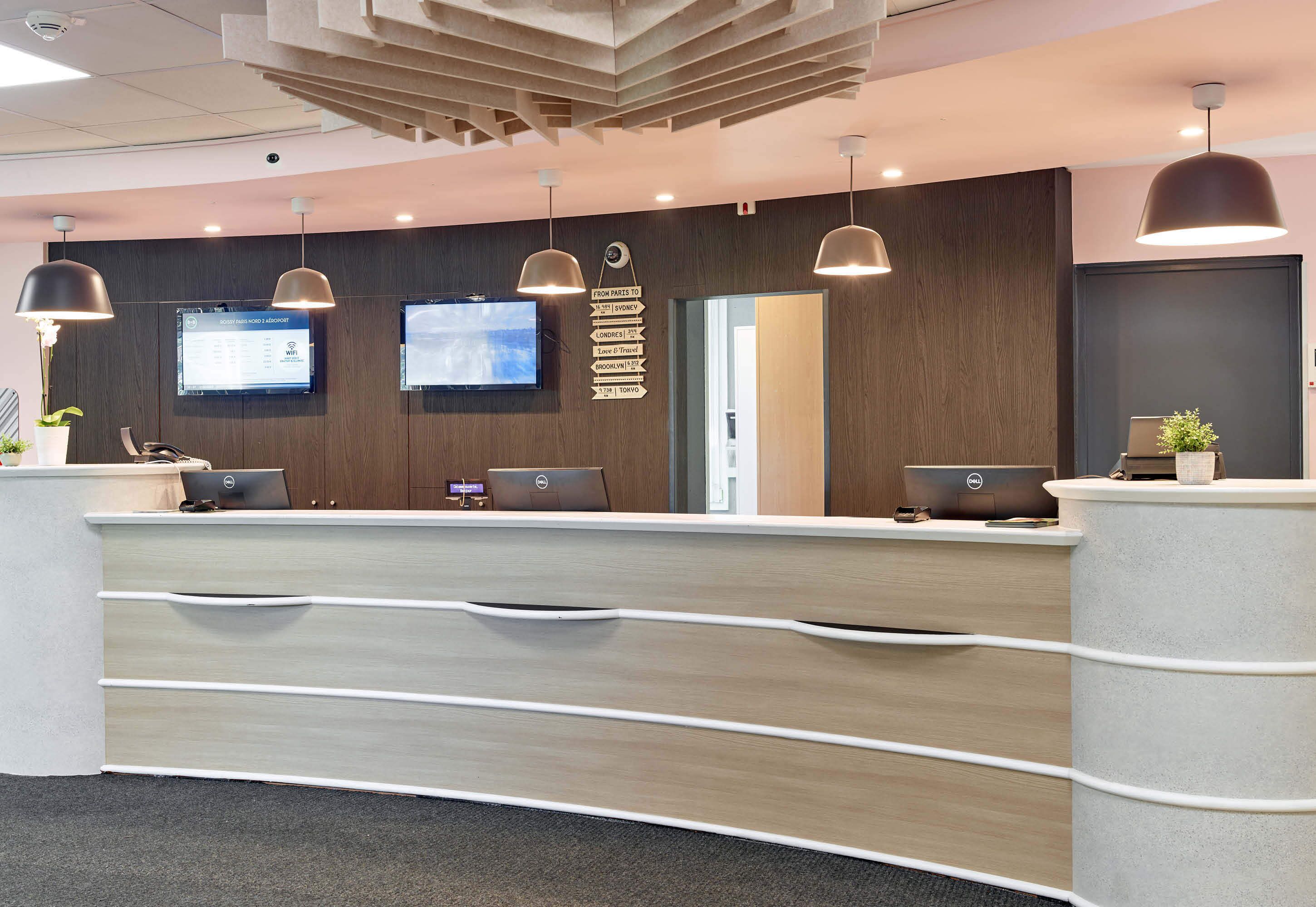 Un mostrador de recepción moderno con dos monitores, un cartel con destinos turísticos y un panel de pared de madera.