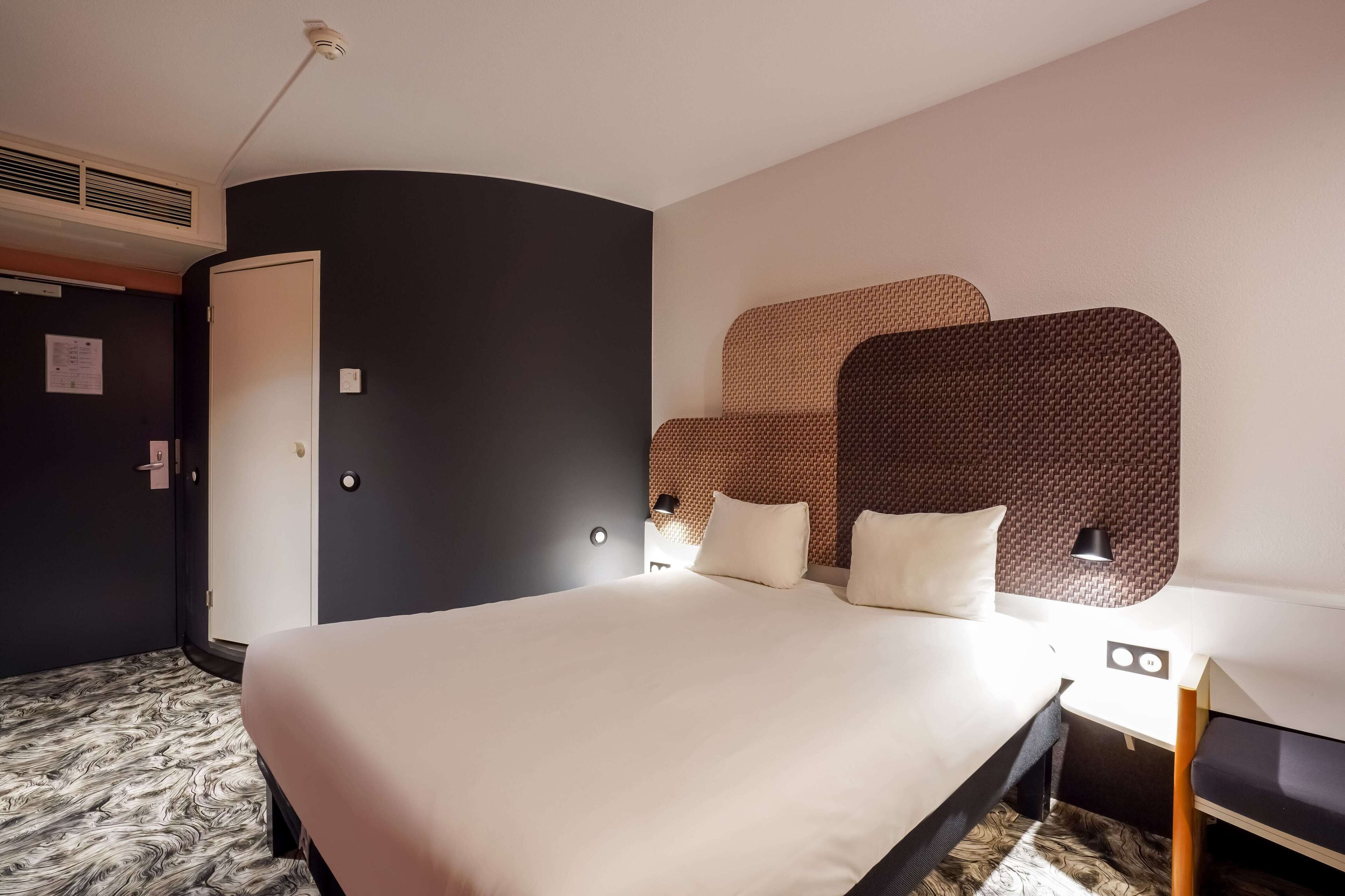 Una habitación de hotel moderna con una cama grande, un armario y un cabecero con un diseño texturizado.