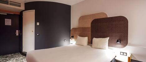 Una habitación de hotel moderna con una cama grande, un armario y un cabecero con un diseño texturizado.