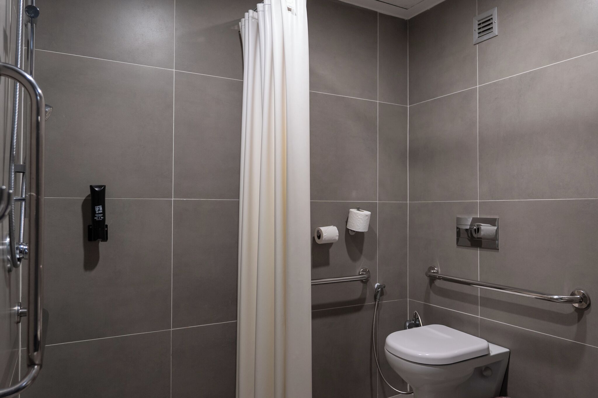 A bathroom with a shower, toilet, and handrails.