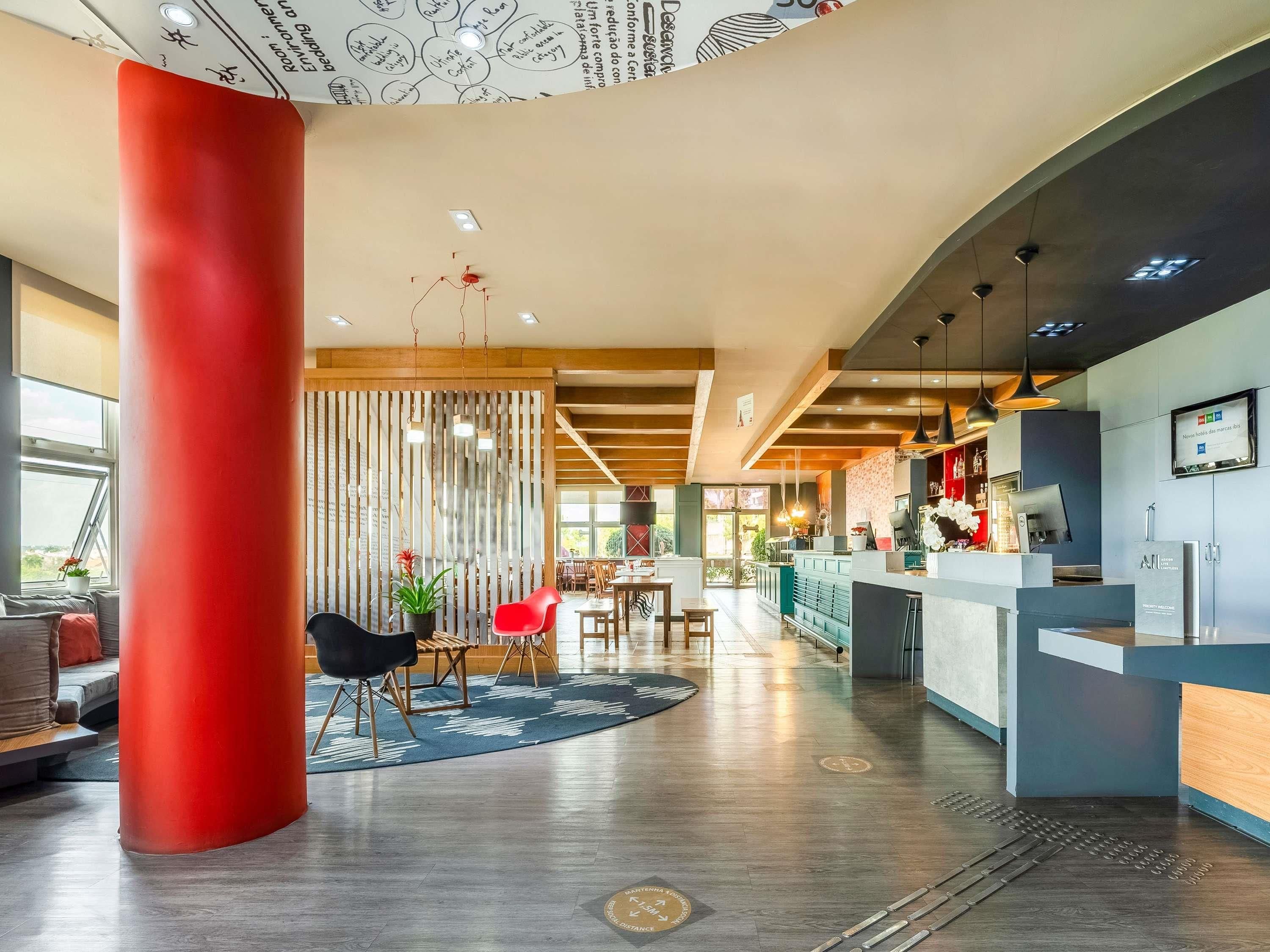 Un moderno vestíbulo de hotel con una recepción, una zona de estar y un pilar rojo grande.