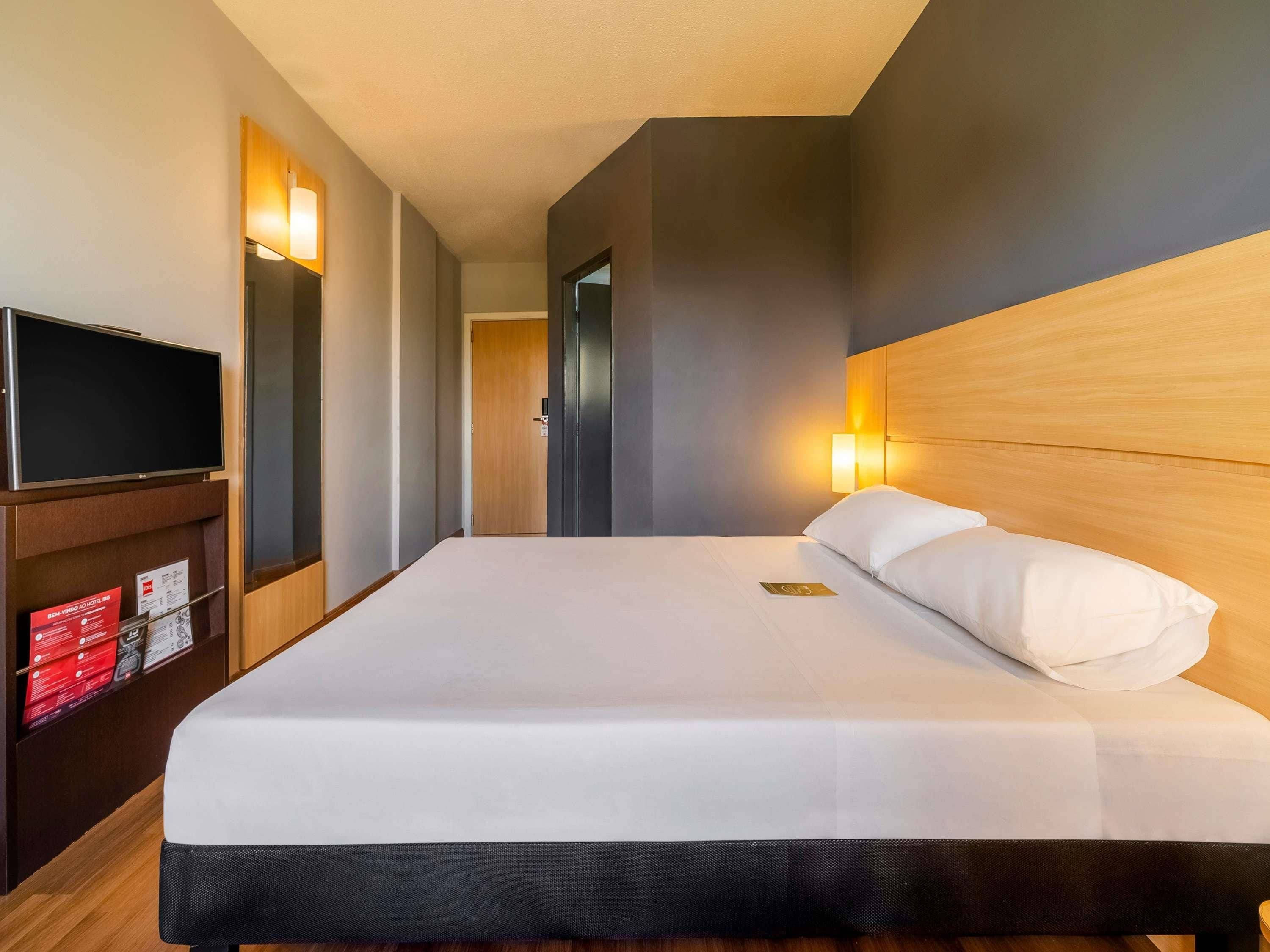 Habitación de hotel con cama, televisor y lámpara fijada a la pared.