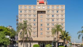 A multi-story hotel with a prominent 'ibis' sign, featuring a symmetrical facade with evenly spaced windows and a central entrance.