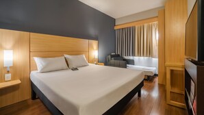 A hotel room with a large bed, a desk, a chair, a television, and a window with curtains. - ibis Sorocaba (Sorocaba)