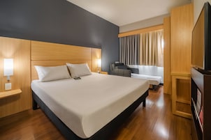 Habitación de hotel con una cama grande, un escritorio, una silla, un televisor y una ventana con cortinas.