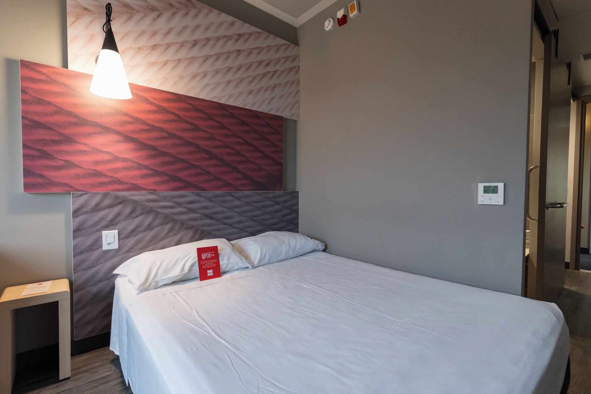Habitación de hotel con una cama, una mesita de noche, una lámpara fijada a la pared y un diseño de pared con textura.