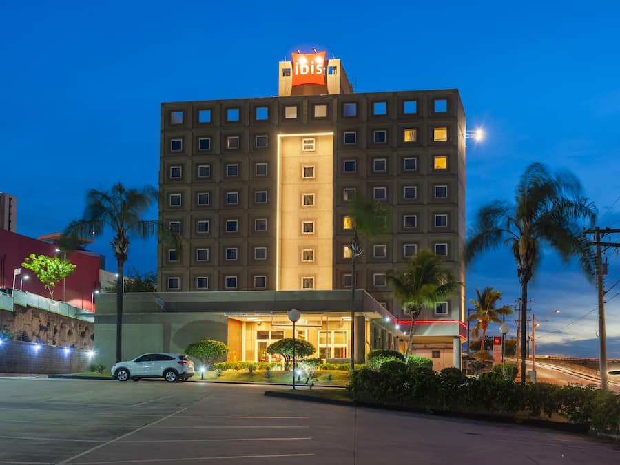 A multi-story hotel with a prominent "ibis" sign, a parking lot, and palm trees.