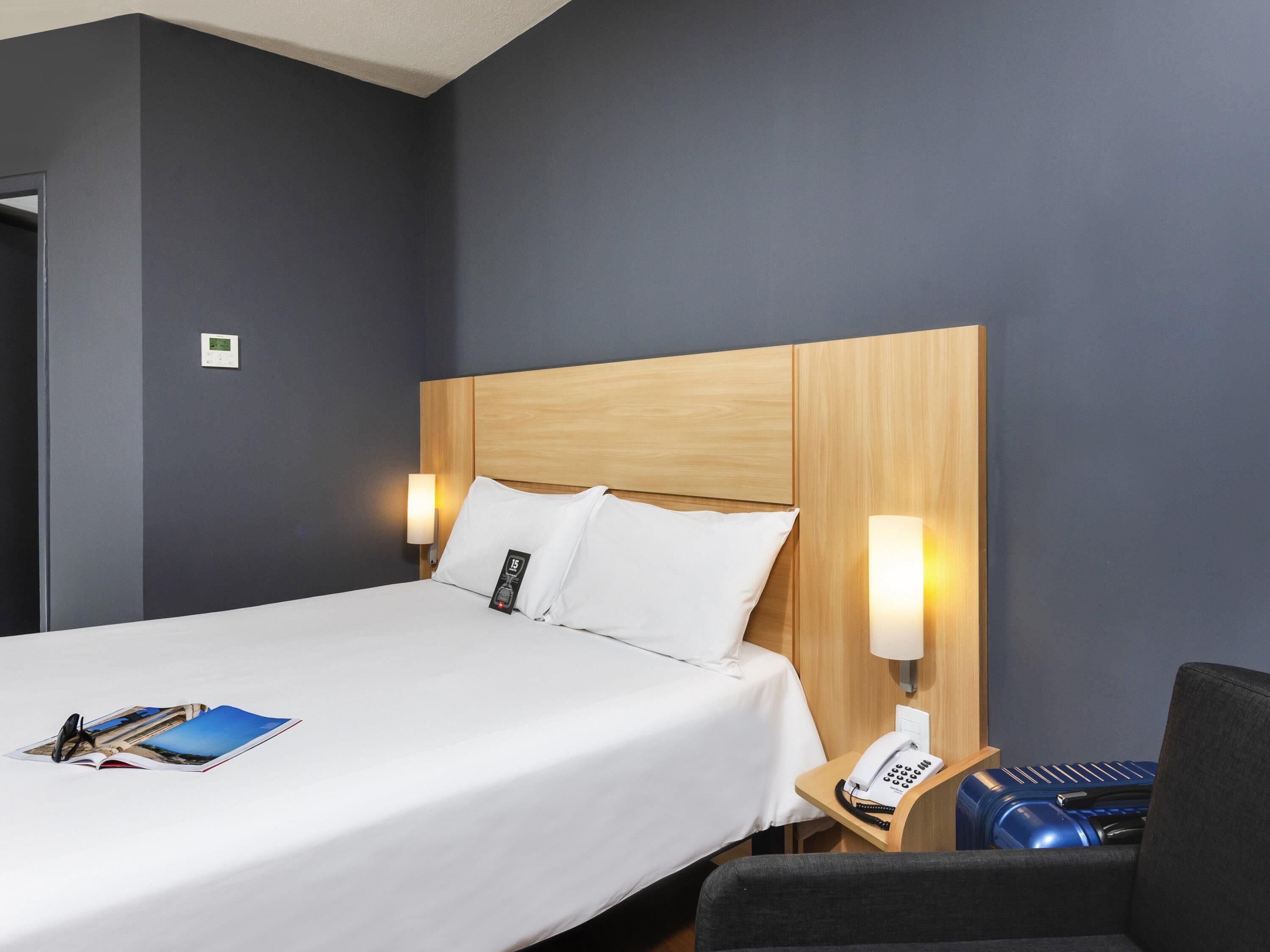 Quarto de hotel com uma cama grande, abajures, telefone e uma cadeira.
