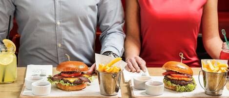 Une scène de restaurant où deux personnes sont assises à une table, chacune ayant devant elle un hamburger et une portion de frites.