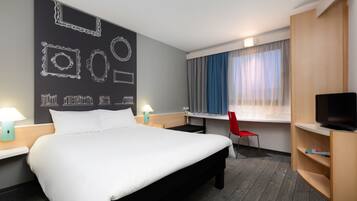 A hotel room with a large bed, a desk with a chair, a TV, and a window with curtains.