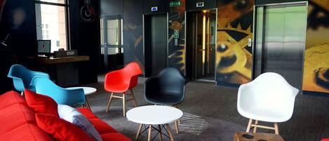 A modern lobby with red and blue seating, a reception desk, and elevators.