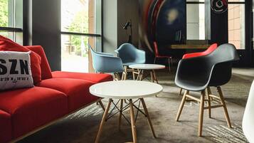 Un espace détente moderne avec un canapé rouge, des fauteuils bleus et noirs, et une petite table ronde.