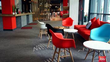 A modern hotel lobby with red and blue seating, a reception desk, and large windows.