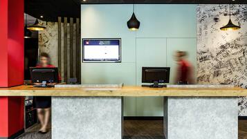 A reception desk with two computer monitors, a wall-mounted TV, and a patterned wall.