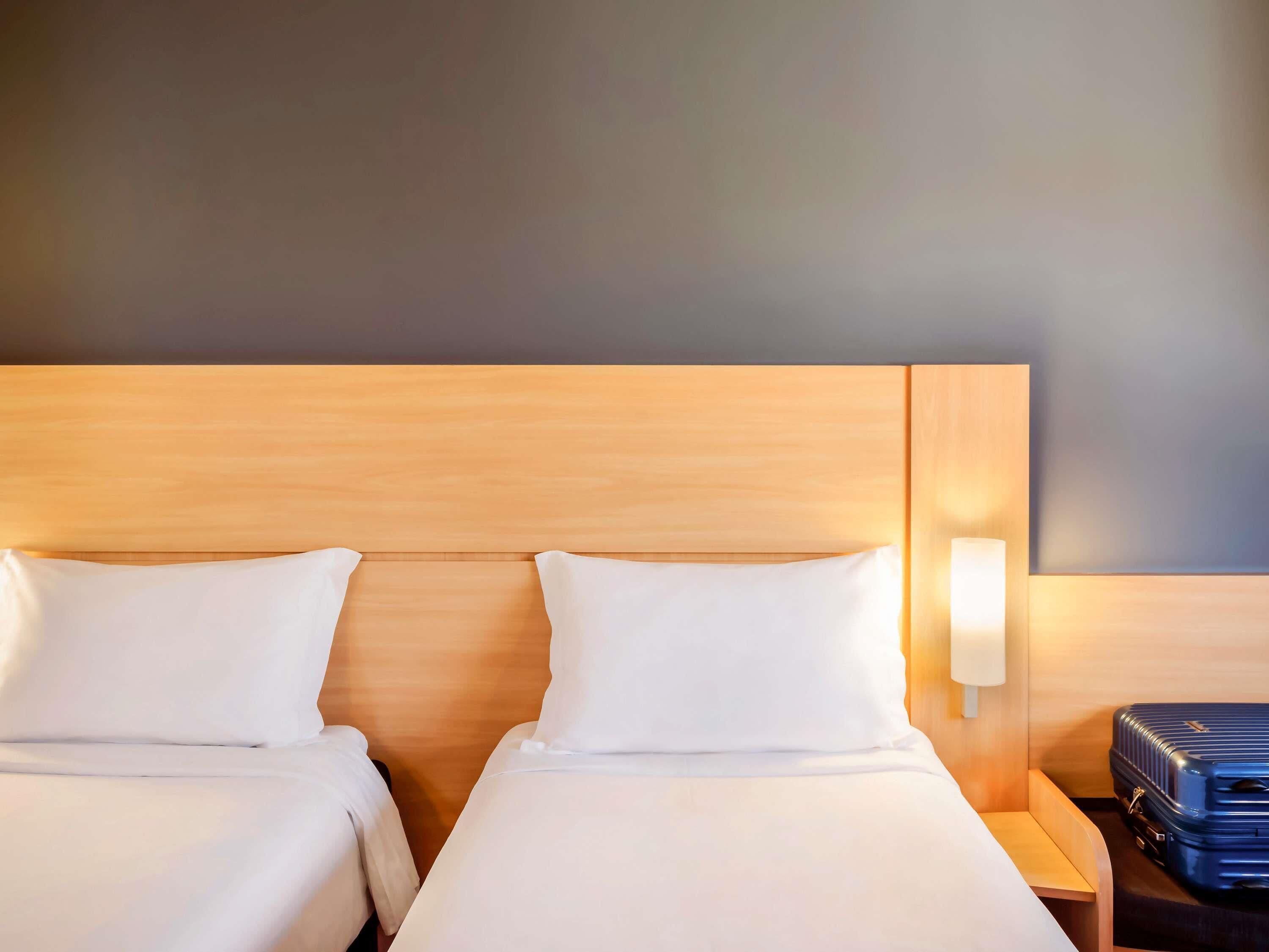 Una habitación de hotel con dos camas, una mesita de noche, una lámpara y una maleta.