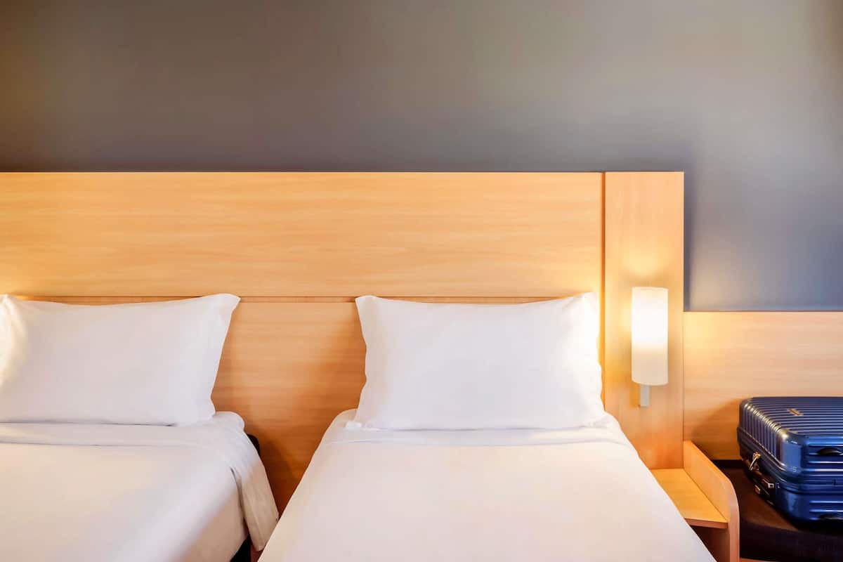 Una habitación de hotel con dos camas, una mesita de noche, una lámpara y una maleta.