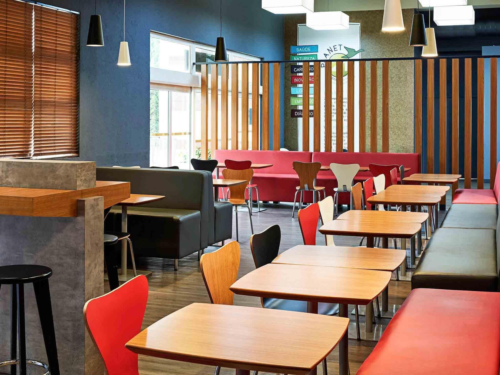 A modern restaurant interior with wooden tables, red and black chairs, and a red booth seating area.
