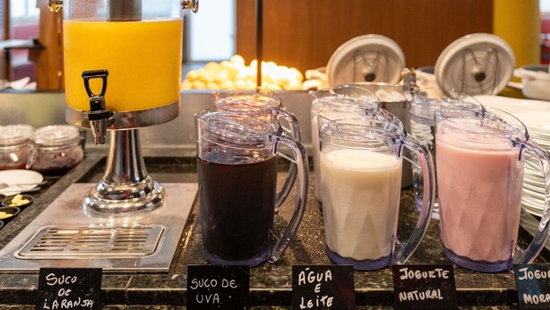 A beverage station with a juicer, pitchers of different drinks, and labels indicating the types of beverages available. - ibis Paulinia (Paulinia)