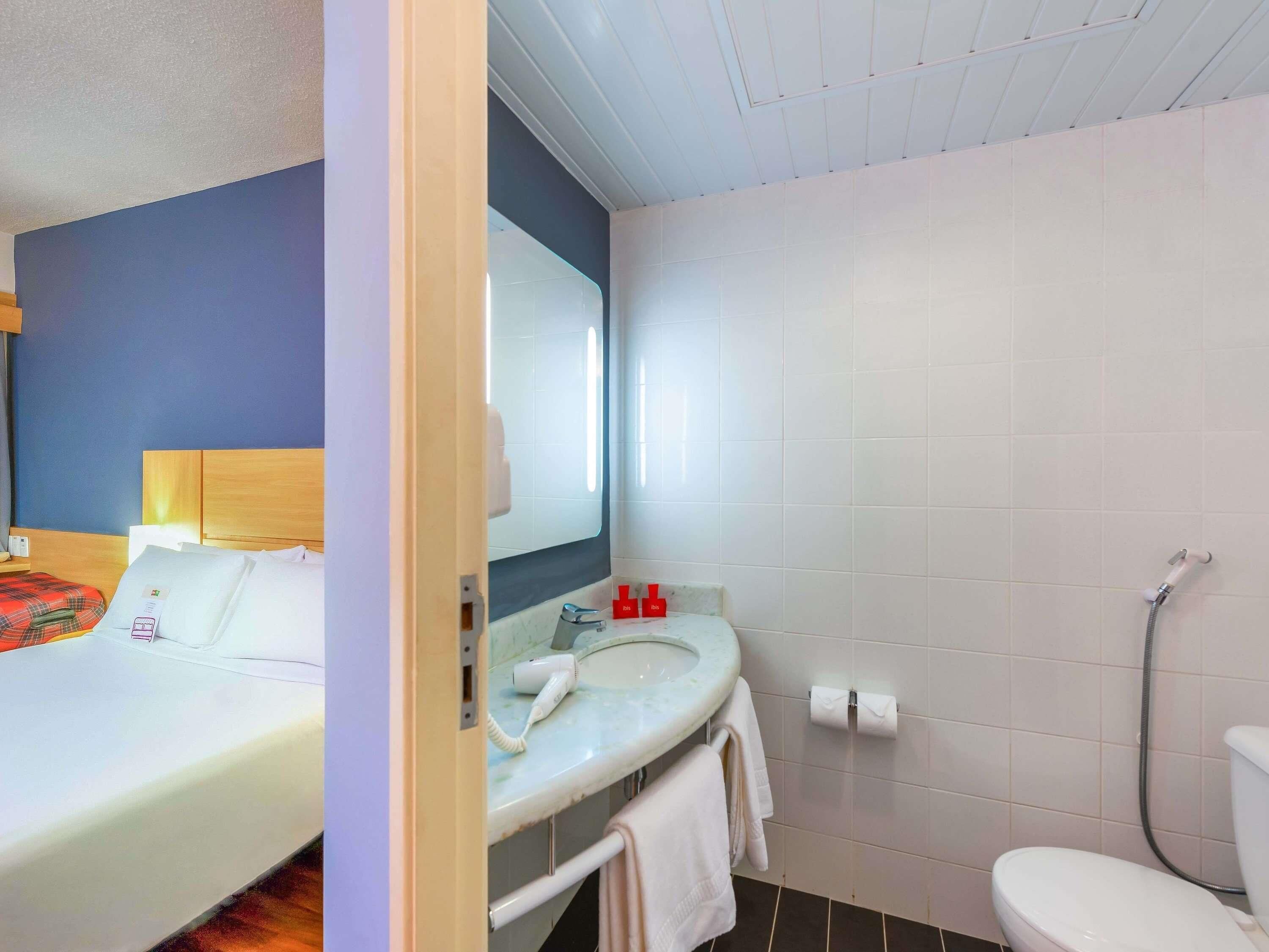 A hotel room with a bed, a bathroom with a sink, mirror, and toilet.