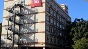 A building with a prominent red 'ibis' sign, multiple floors, and a fire escape on the left side. - ibis Paulinia (Paulinia)