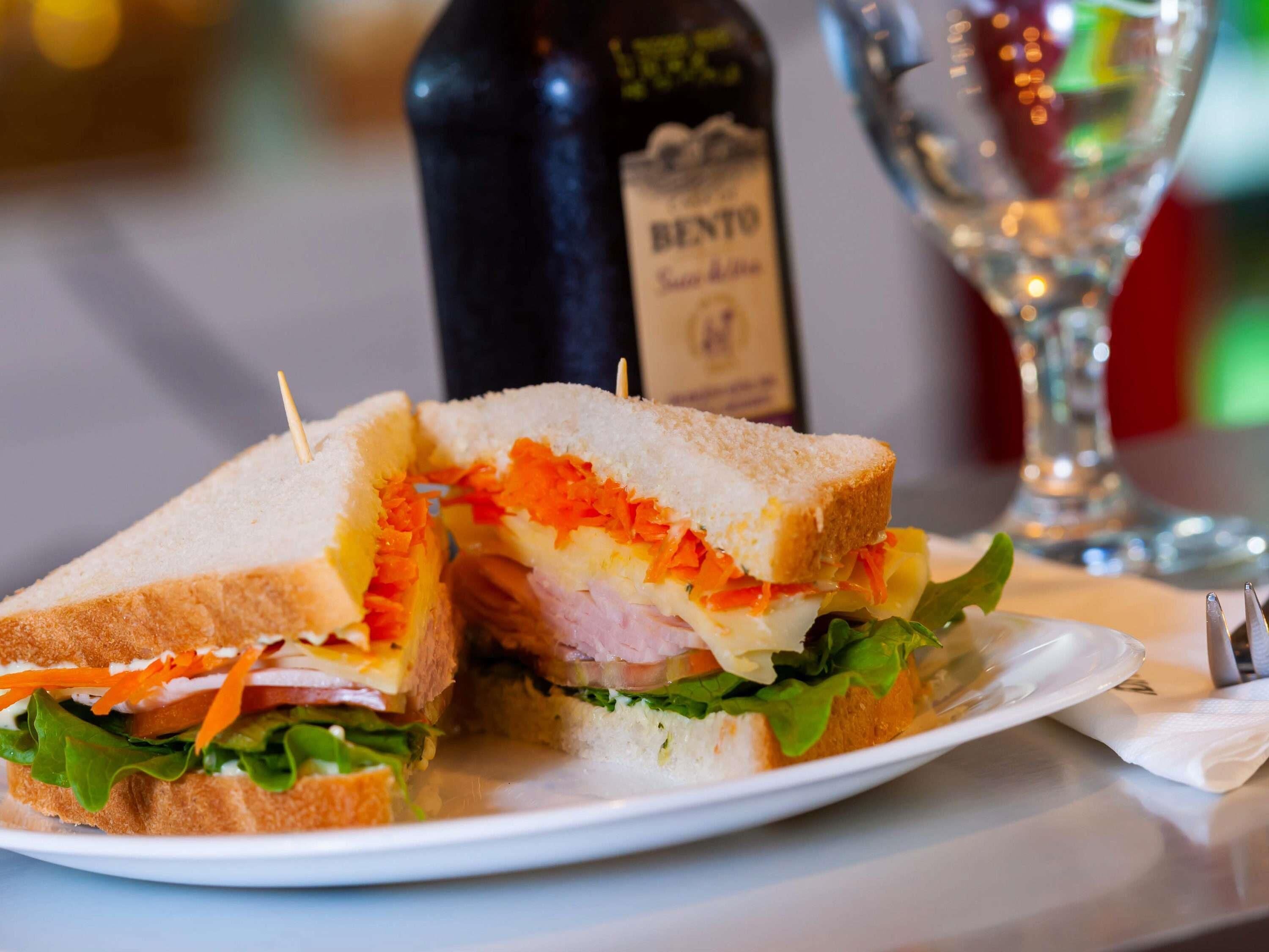 Un sándwich en un plato con una botella y una copa al fondo.