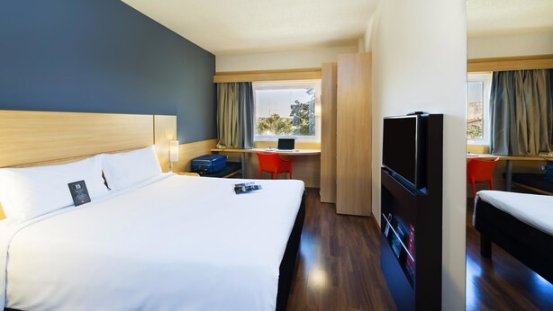 A hotel room with a large bed, a desk with a laptop, a TV, and a suitcase. - ibis Paulinia (Paulinia)