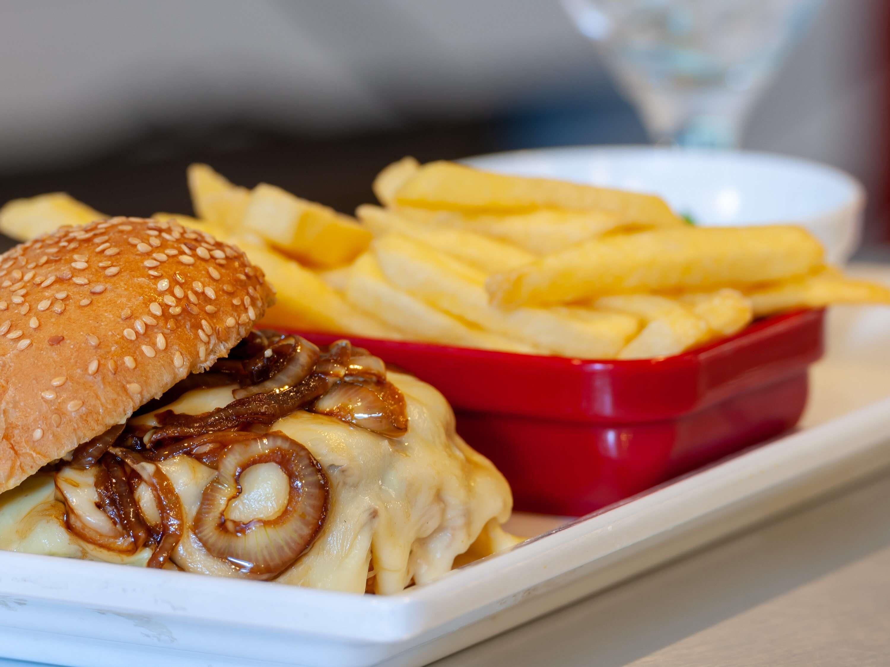 A meal consisting of a burger with cheese and onions, French fries, and a small red container, likely containing a dipping sauce.