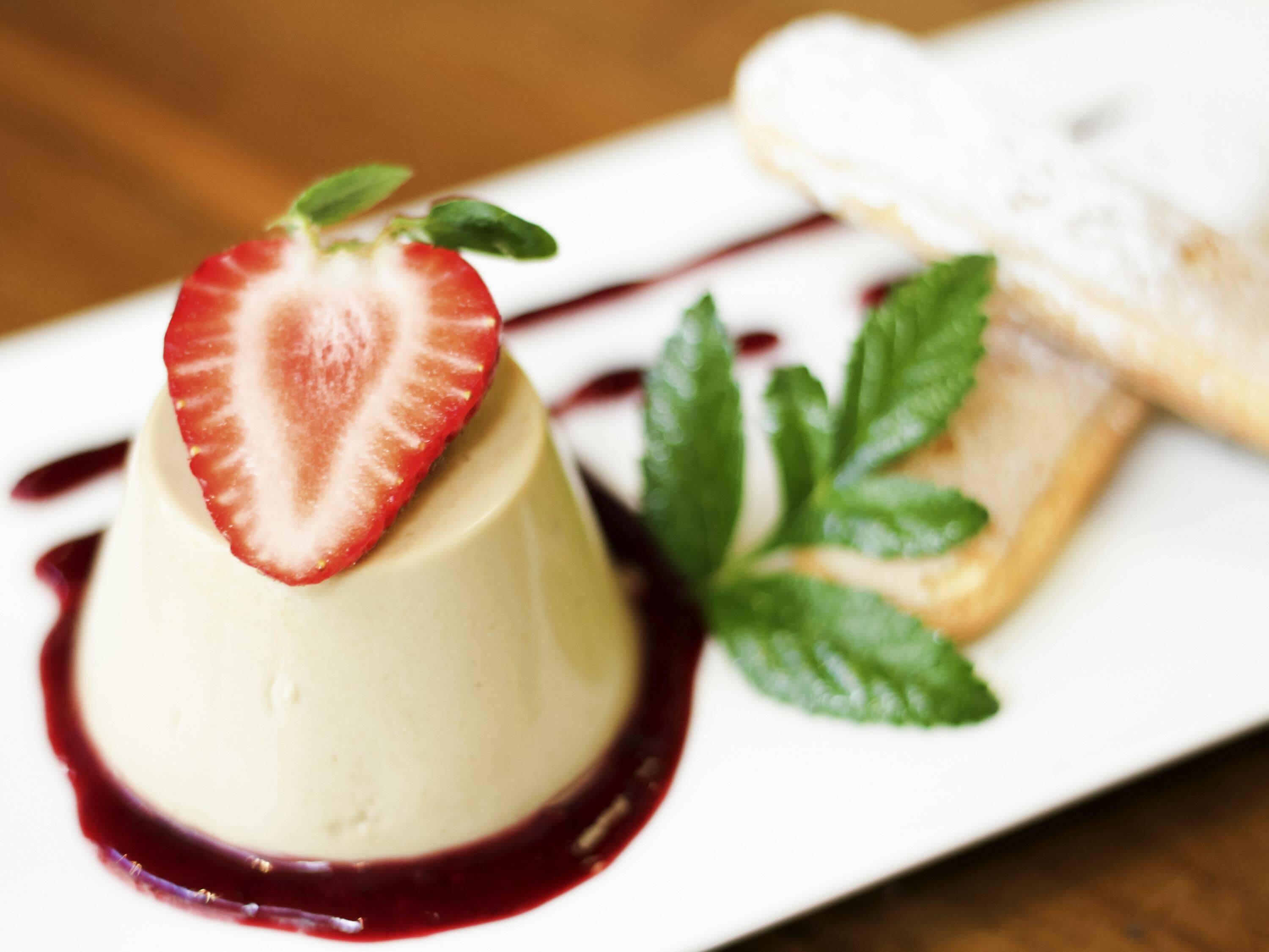A dessert with a strawberry on top, a berry sauce, and a pastry on a white plate.
