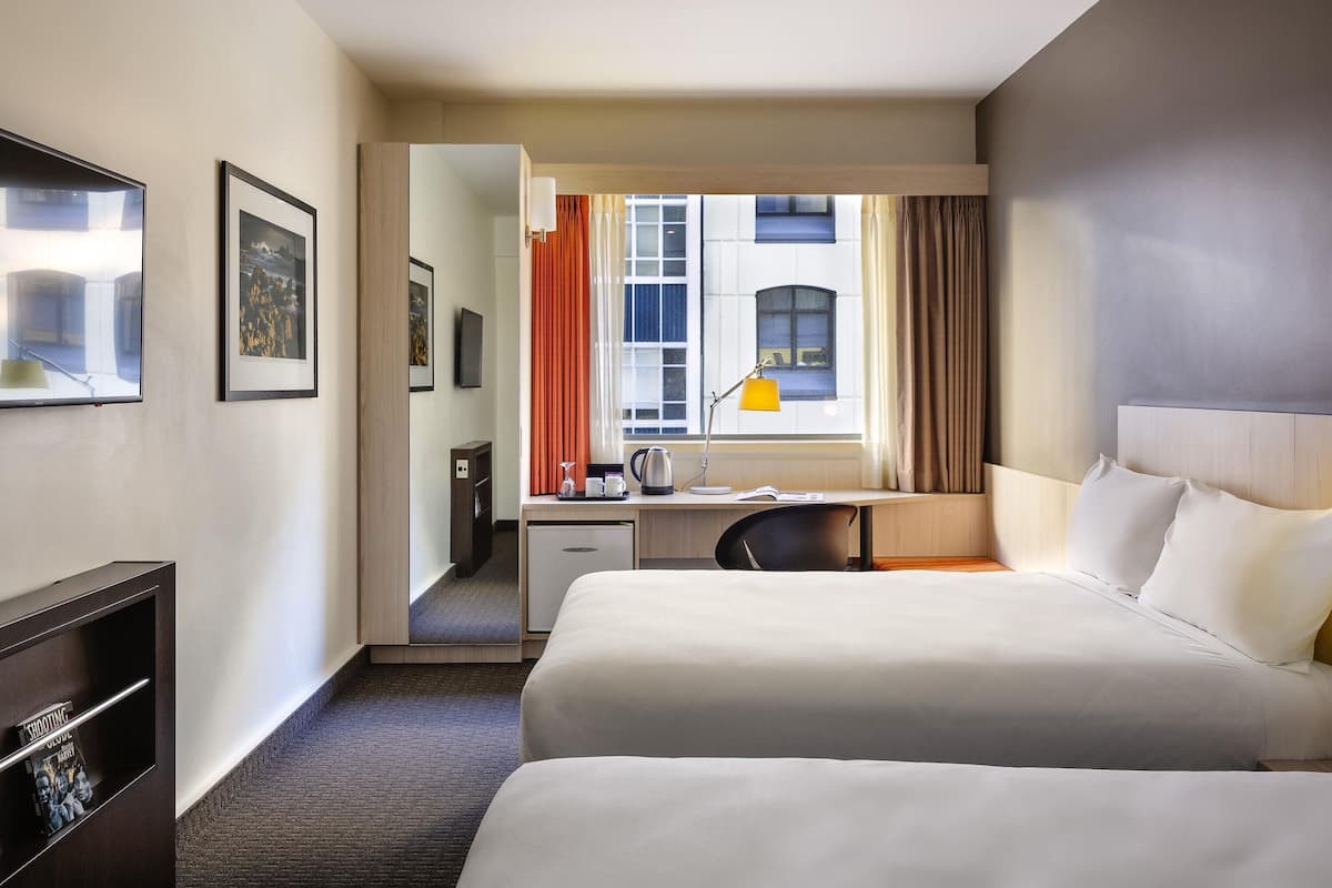 A hotel room with two beds, a desk, a chair, a TV, and a window with curtains.