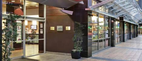 The exterior of an ibis hotel with a modern design, featuring a prominent red sign, glass doors, and potted plants.