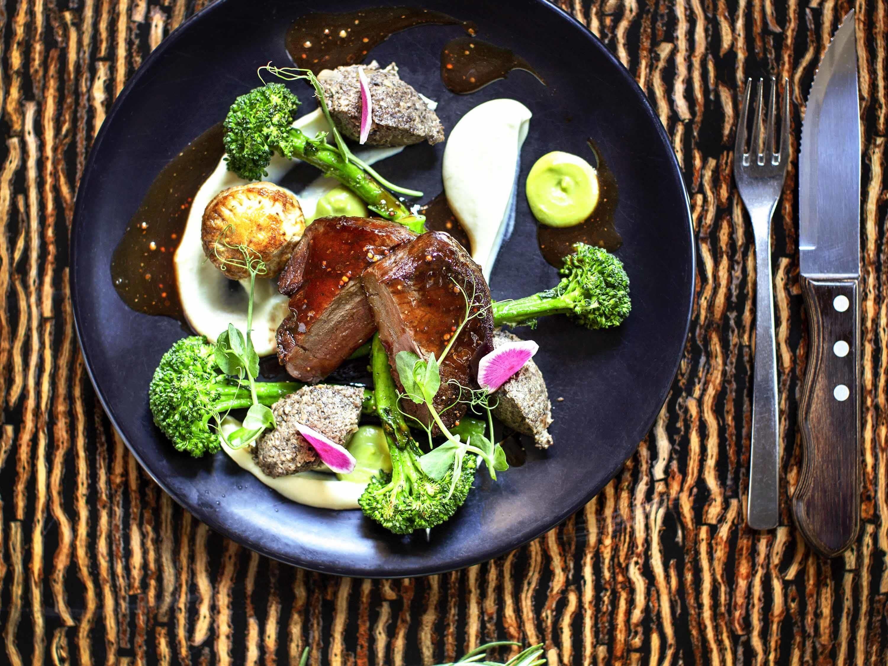 A plate of food with meat, vegetables, and sauce on a dark plate.