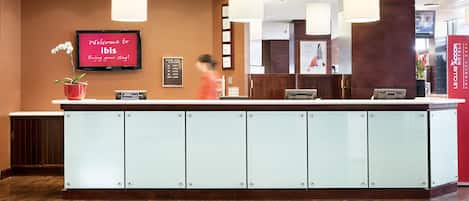 A reception area with a modern design, featuring a large reception desk, a flat-screen TV displaying a welcome message, and a potted orchid.