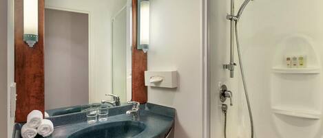 A bathroom with a dark granite sink, a mirror, a handheld showerhead, and a white towel rack.