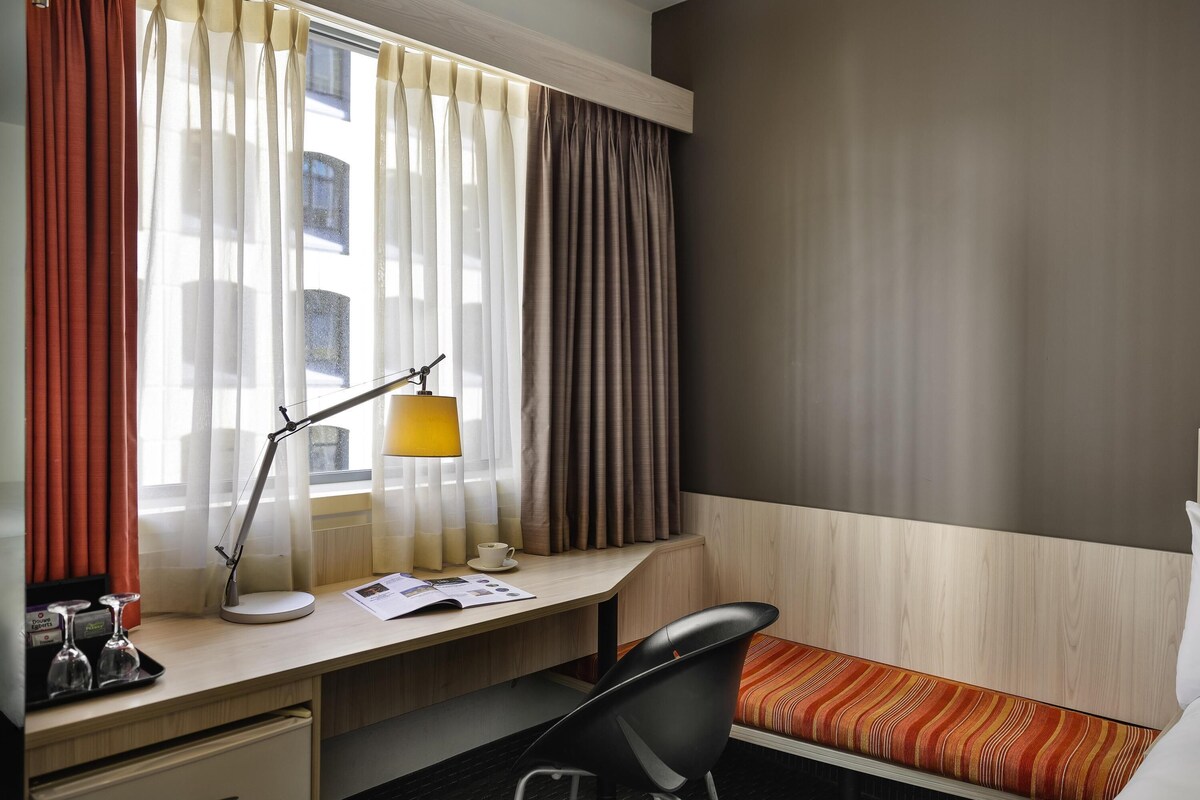 Una habitación de hotel con escritorio, silla y cama con manta a rayas.