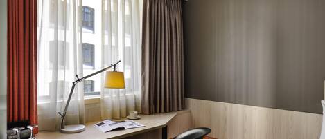 A hotel room with a desk, chair, and a bed with a striped blanket.