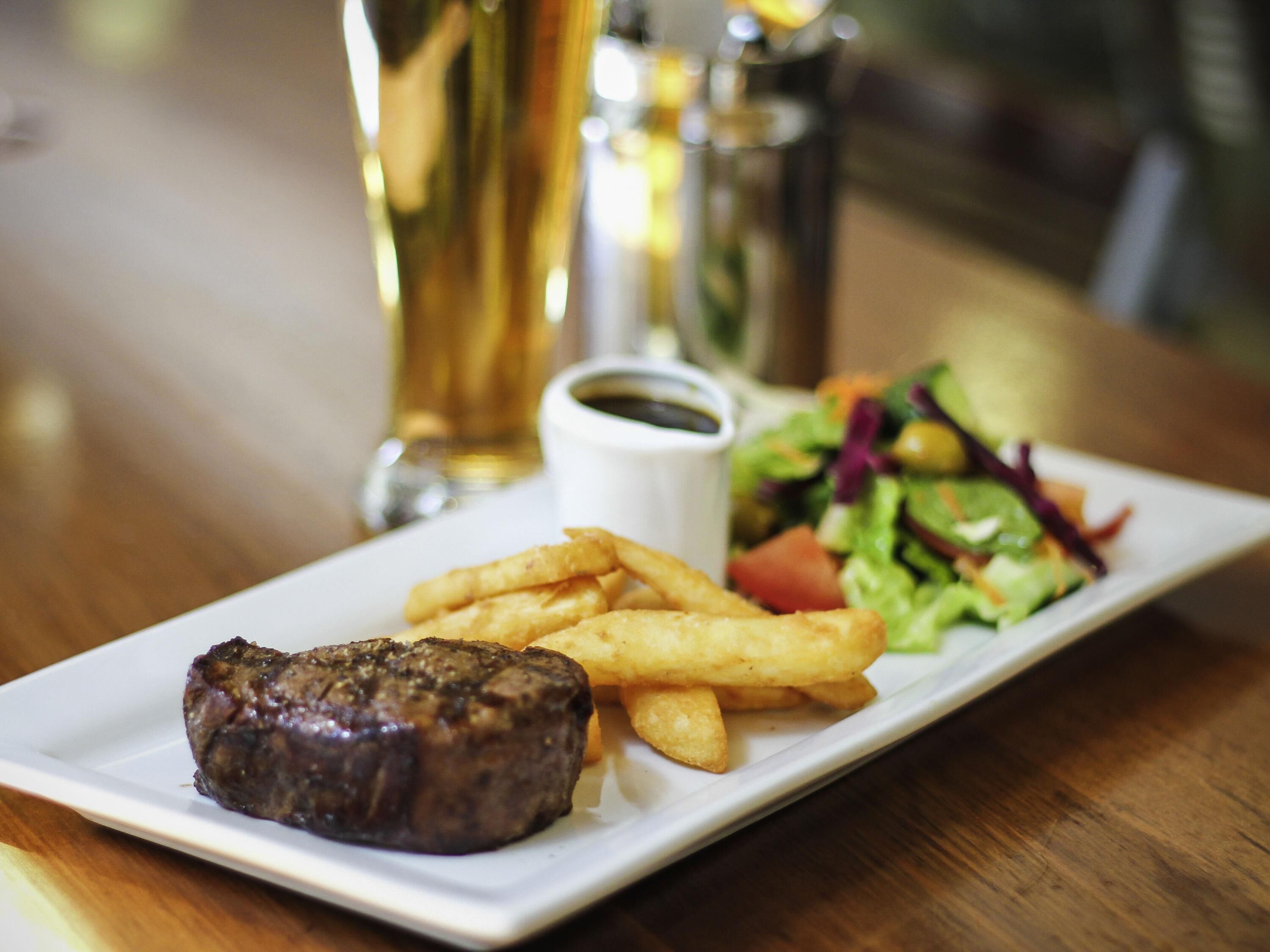 Un plato con un filete, papas fritas y una ensalada sobre una mesa.